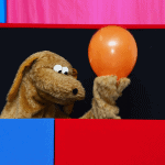 Quiz Worx. Picture shows a dog puppet holding up an orange balloon in their show.